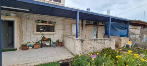 Dark blue aluminum pergola running along a stone house with potted plants