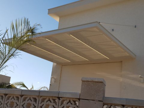 Cream aluminum pergola with integrated LED lines, fixed above a garage and held by tension rods