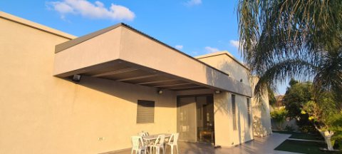 Dark aluminum pergola projecting from a beige house over an outdoor dining area
