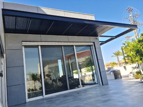 Wide view of a dark grey aluminum pergola above a patio and large glass doors
