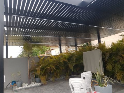 Dark aluminum louvre pergola over a paved courtyard with planters