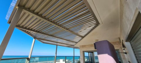 Dark aluminum pergola over a balcony with a glass balustrade and a sea view