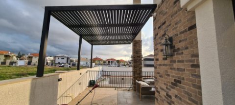 Dark aluminum pergola beside a brick pillar on a terrace with an open view