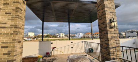 Dark aluminum pergola between brick-clad pillars on an elevated terrace