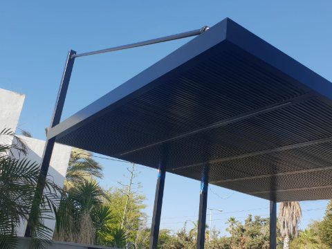 Dark grey aluminum pergola with slim posts and a tension rod, seen from below with palm trees behind