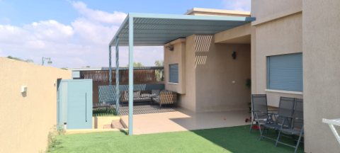 Grey-green aluminum pergola on posts over a patio with outdoor chairs and lawn