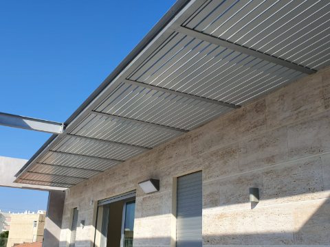 Grey aluminum louvre pergola running along a stone-clad facade