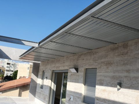 Grey aluminum louvre pergola attached to a stone-clad house, seen from the corner
