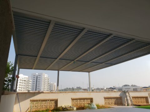 Grey aluminum pergola on a roof terrace with patterned balustrade walls and a city view