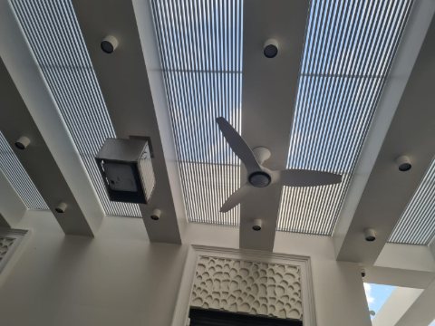 Pergola ceiling detail: white aluminum louvres with downlights, a ceiling fan and a speaker