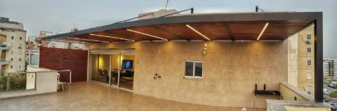 Wide view of a rooftop aluminum pergola with a wood-look roof and downlights