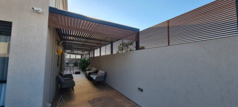 Wood-look aluminum pergola and privacy screen on a roof terrace with outdoor seating
