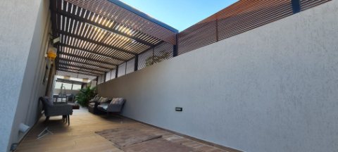 Rooftop aluminum pergola with wood-look slats and a matching privacy screen along a wall