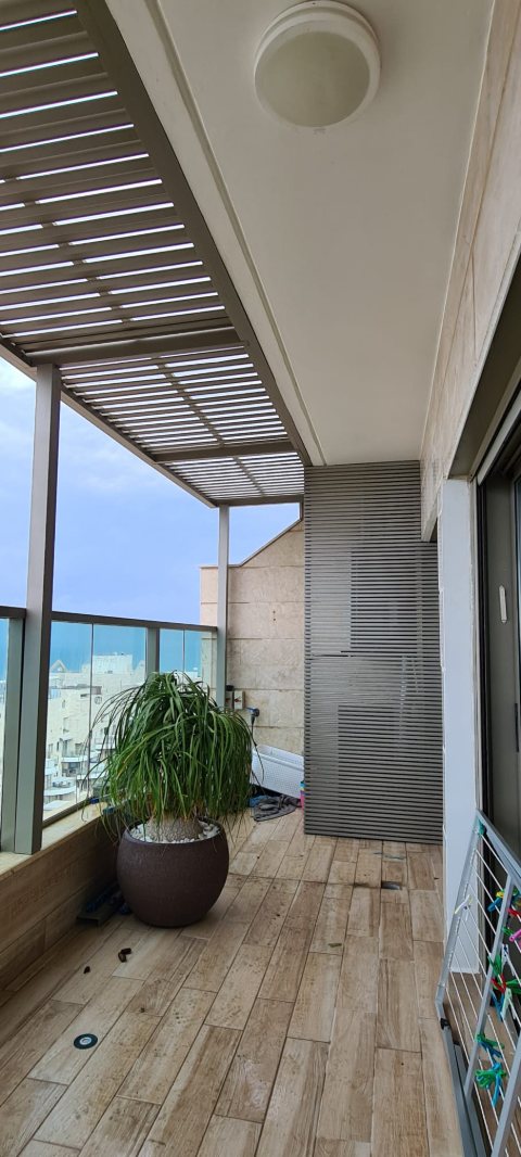 Slatted aluminum pergola over a narrow balcony with timber-look flooring
