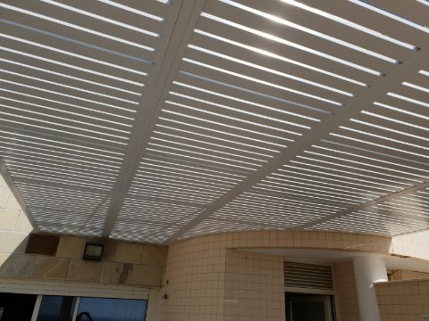 Underside of a white aluminum louvre pergola above a curved tiled wall
