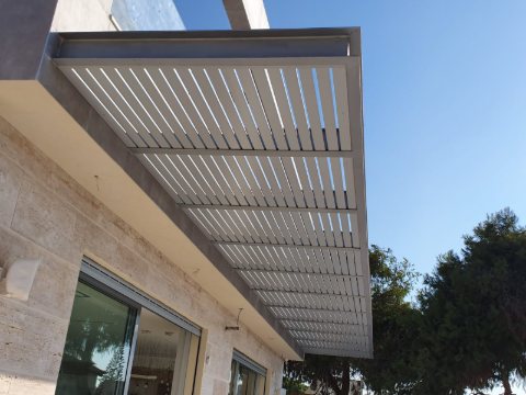 White aluminum louvre pergola attached to a stone-clad house with large windows