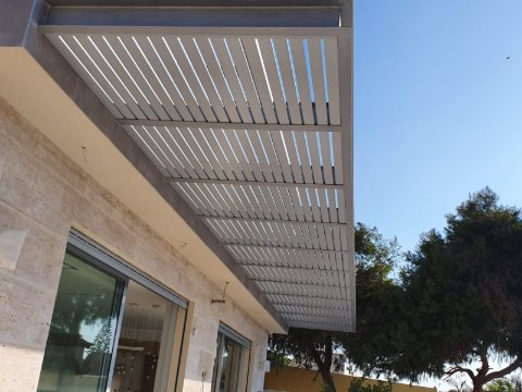 Underside of a white aluminum louvre pergola attached to a stone-clad house
