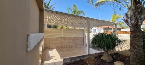 White aluminum pergola over a tiled courtyard with a large potted plant