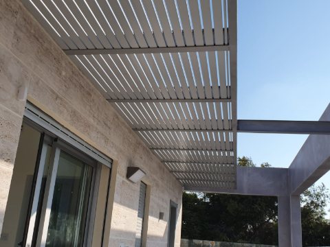 White aluminum slats on a grey beam structure attached to a stone facade