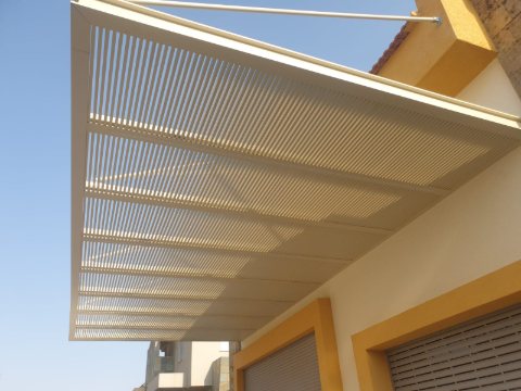 White aluminum slatted pergola fixed to a wall with yellow trim and supported by tension rods