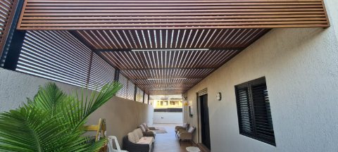 Long wood-look aluminum pergola running along a narrow side yard with outdoor seating
