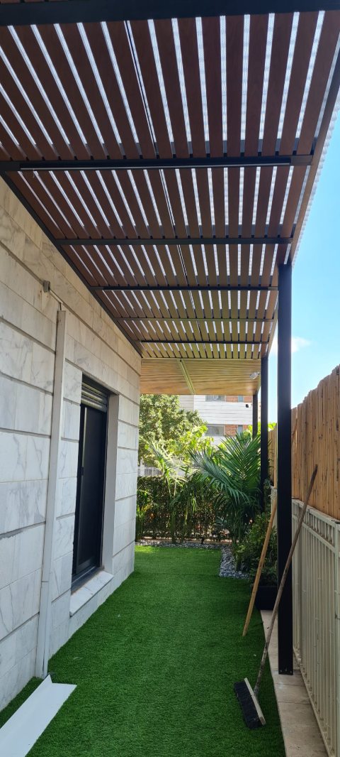 Wood-look aluminum pergola over a narrow side yard with artificial lawn, portrait view