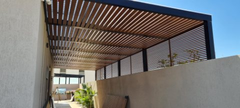 Wood-look aluminum slatted pergola with a dark frame and matching privacy screen on a terrace